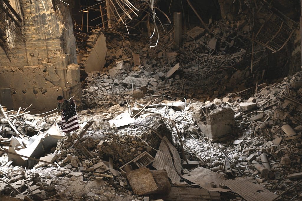 A soldier carries an American flag through the rubble inside Saddam Hussein's Victory over America palace, Sept. 11, at Victory Base Complex, Iraq. Soldiers were given the opportunity to pay tribute to the victims of the 9/11 attacks by visiting and flying flags over the palace, which U.S. forces destroyed in 2003 after Saddam Hussein began construction to signify the "defeat" of America.