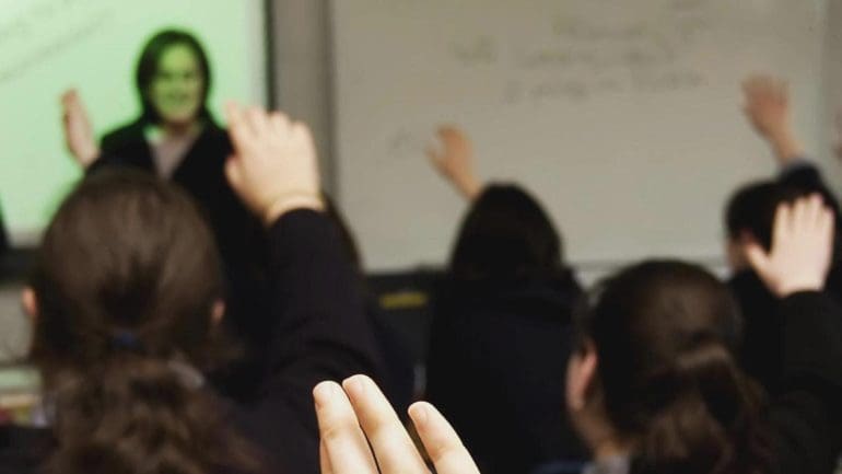 A class room with school children raising their hands