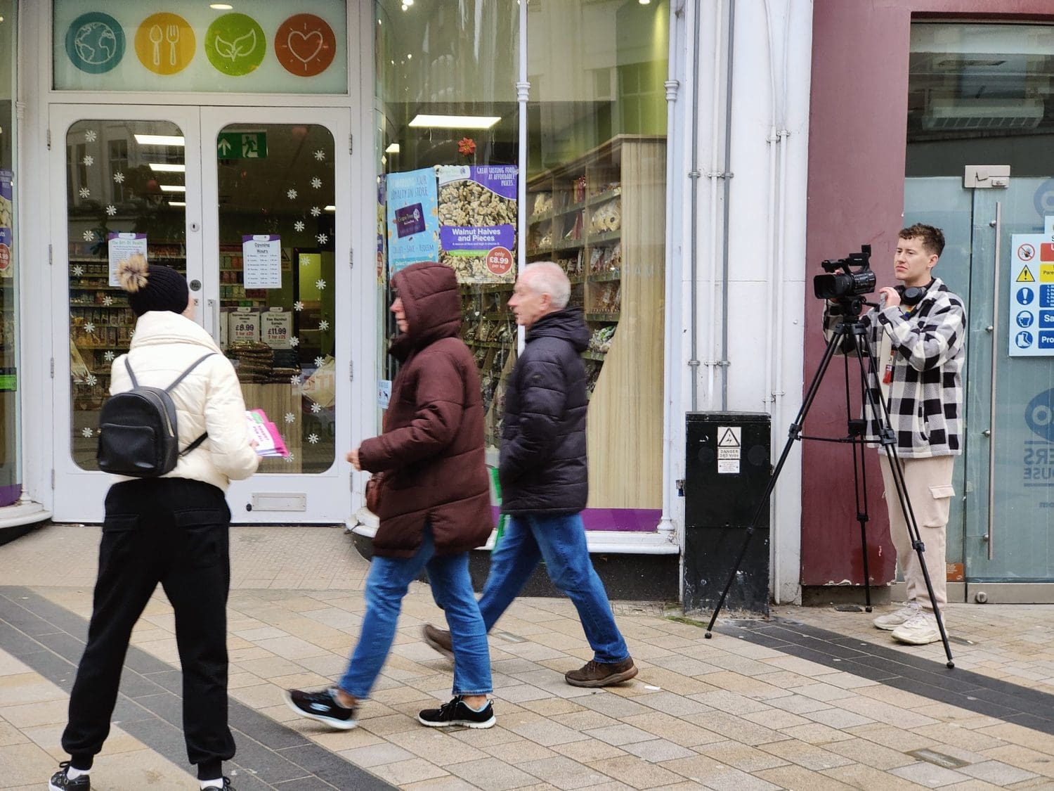 A street scene with a woman on the left handing a couple a banner while someone films them all