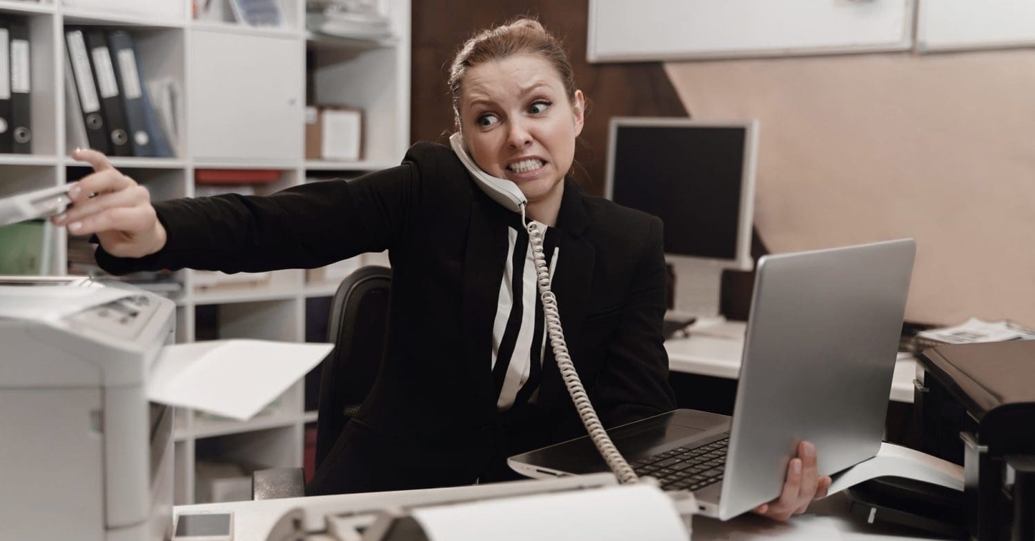 employee looking stressed with a laptop and photcopier