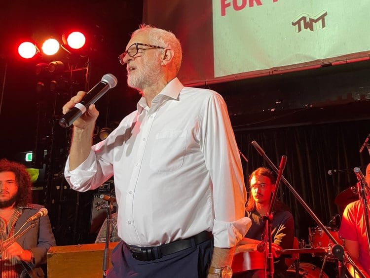 Jeremy Corbyn holding a mic in front of a band