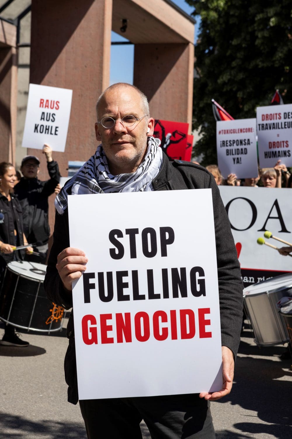 Protester at Glencore AGM with a placard that reads: Stop fuelling genocide.