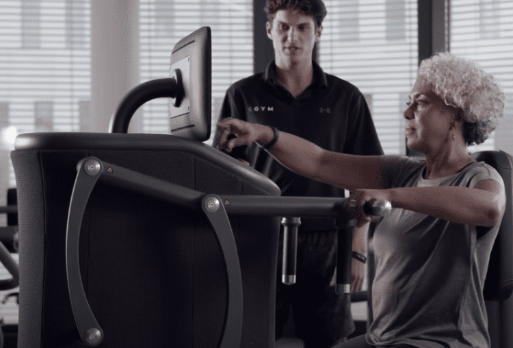 Lady uses EGYM equipment with an EGYM trainer behind long Covid exercise programme Northamptonshire