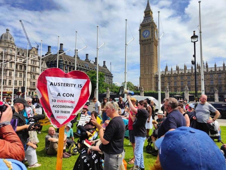 A group of chronically ill and disabled people protesting at parliament square with Big Ben in the background. It is a sunny day