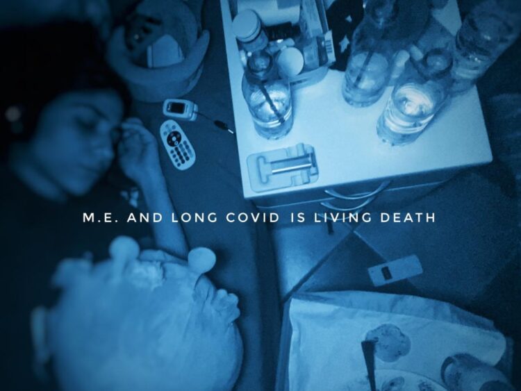 Blue-tinted image of Katiana lying in bed, her bedside table and adjacent mattress stacked out with water bottles, medication, a pulsometer, and a remote control. A plush toy is beside her, and an empty plate with a fork is next to her bed on another small table. Text overlaying it says "M.E. and Long Covid is Living Death" ME/CFS severe ME