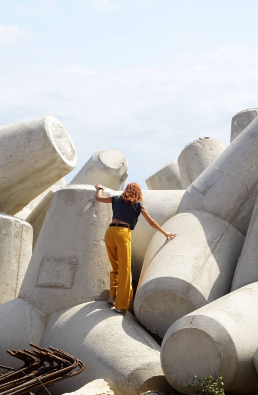 Katiana in yellow trousers and a black top clambering on large tumbling concrete bollards.