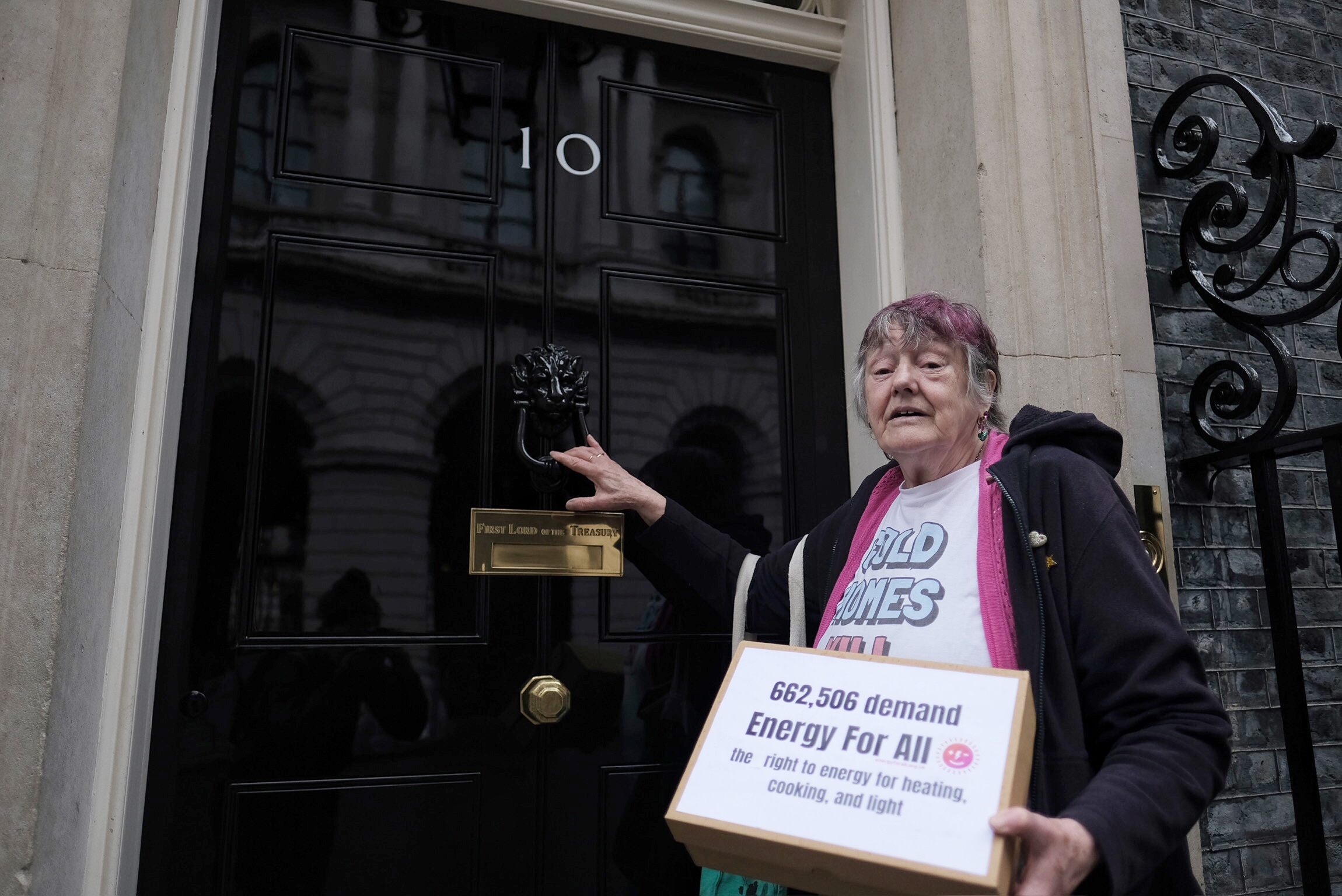 A campaigner preparing to knock the front door at Number 10 Downing Street, with a box carrying the petition reading: 662,506 demand Energy For All - the right to energy for heating, cooking, and light. Energy price cap