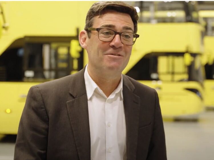 Greater Manchester mayor Andy Burnham standing in front of a fleet of yellow Bee Network buses bus fare cap