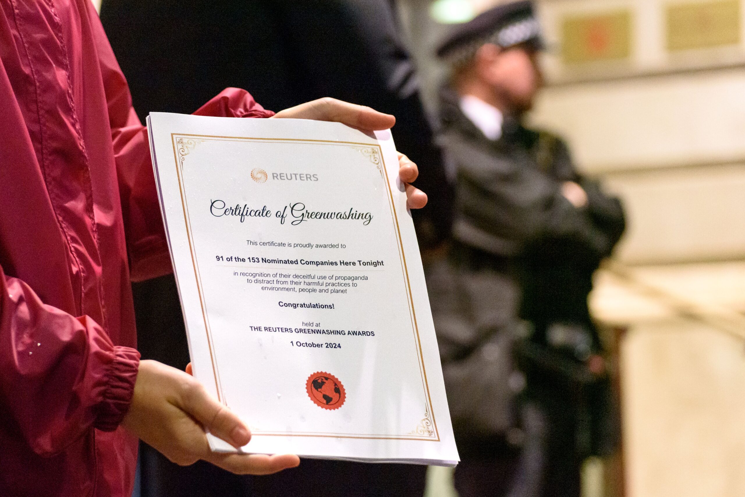 Person holding a 'Certificate of Greenwashing'. It reads: "This certificate is proudly awarded to 91 of the 153 nominated companies here tonight - in recognition of their deceitful use of propaganda to distract from their harmful practices to environment, people, and planet. Congratulations! Held at: The Reuters Greenwashing Awards - 1 October 2024." Reuters Sustainability Awards