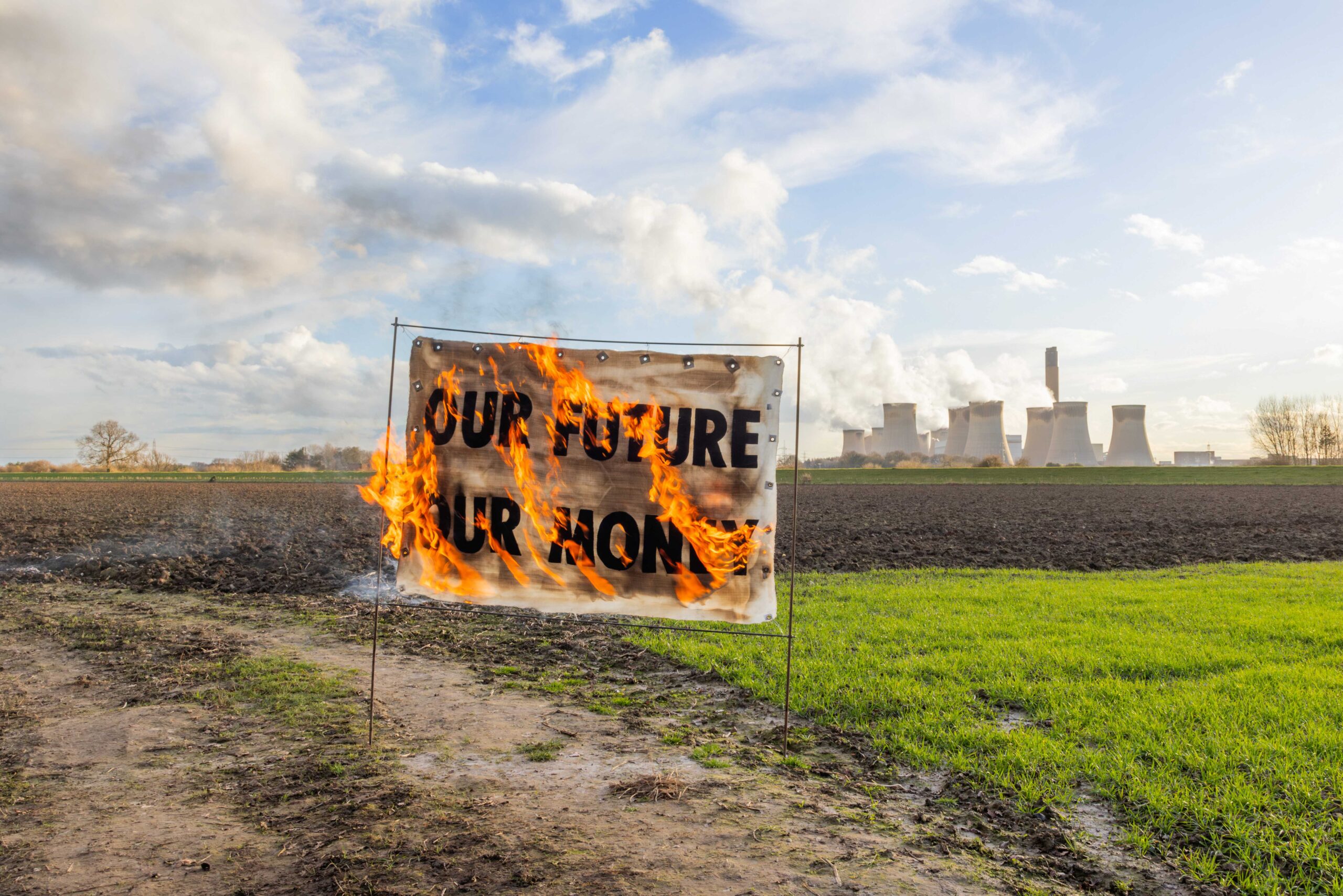 Banner on fire in front of Drax power station that reads: "Our future - our money", with smoke rising in the background from the smokestacks.