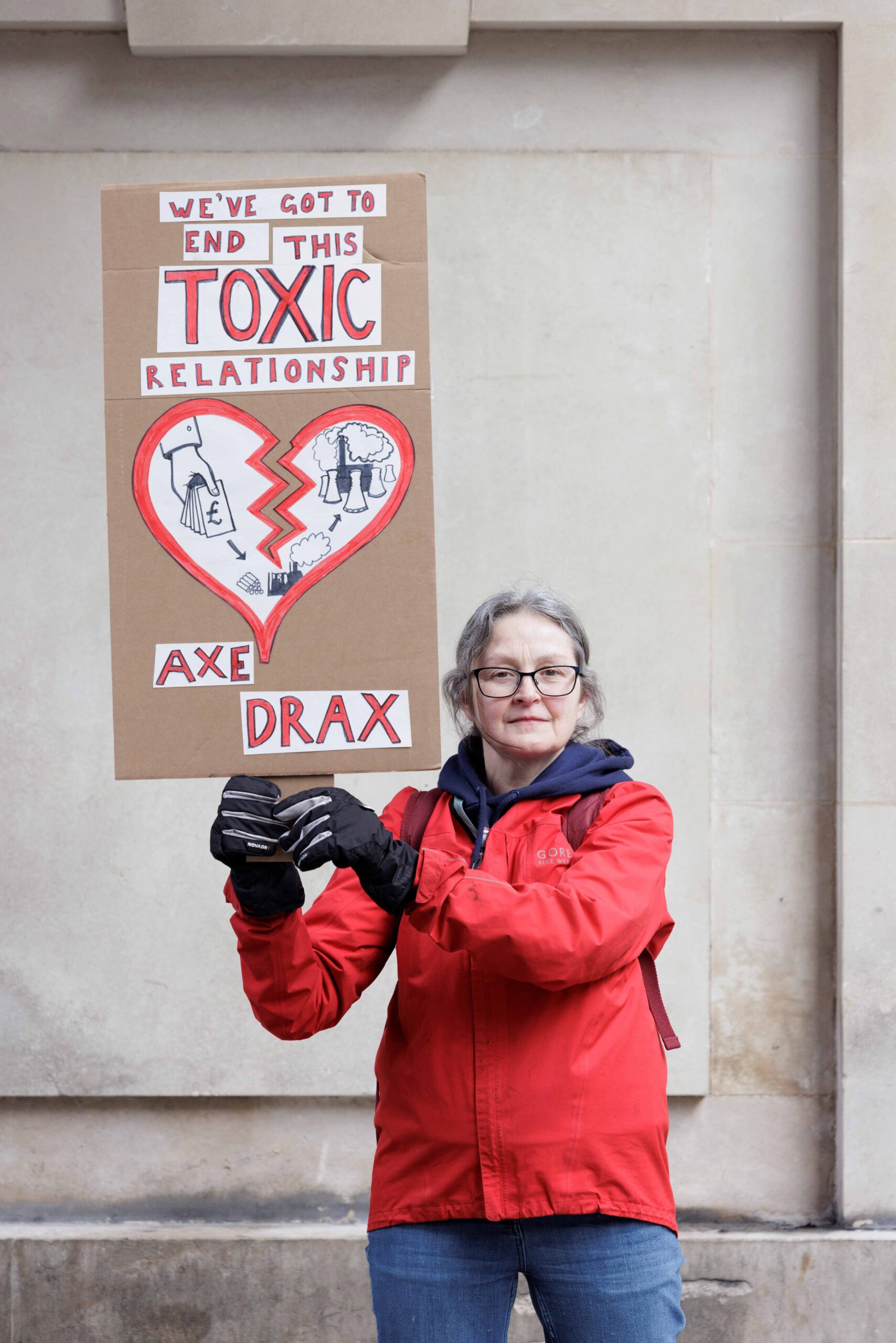 Protester holds up a placard reading: "We've got to end this toxic relationship - Axe Drax." A broken heart with illustrations of a hand holding out cash to Drax's power plant operations, adorns the centre of the placard. 