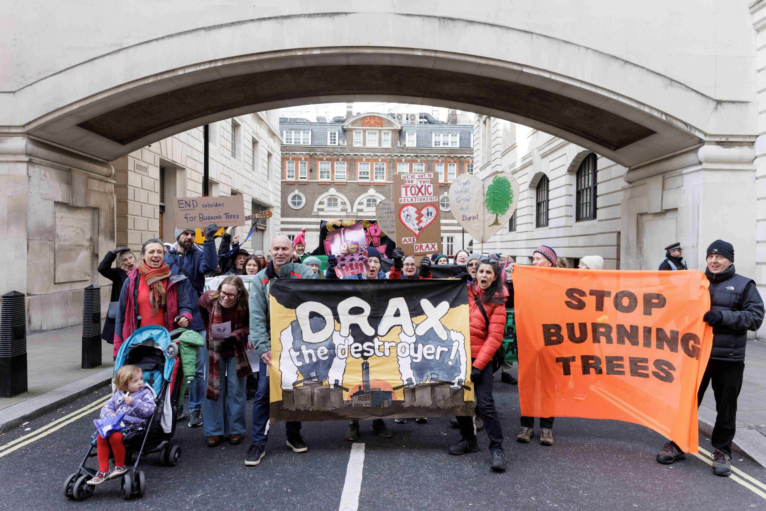 Protesters march with banners and placards. Front banners read: "Drax the destroyer" and "Stop burning trees". 