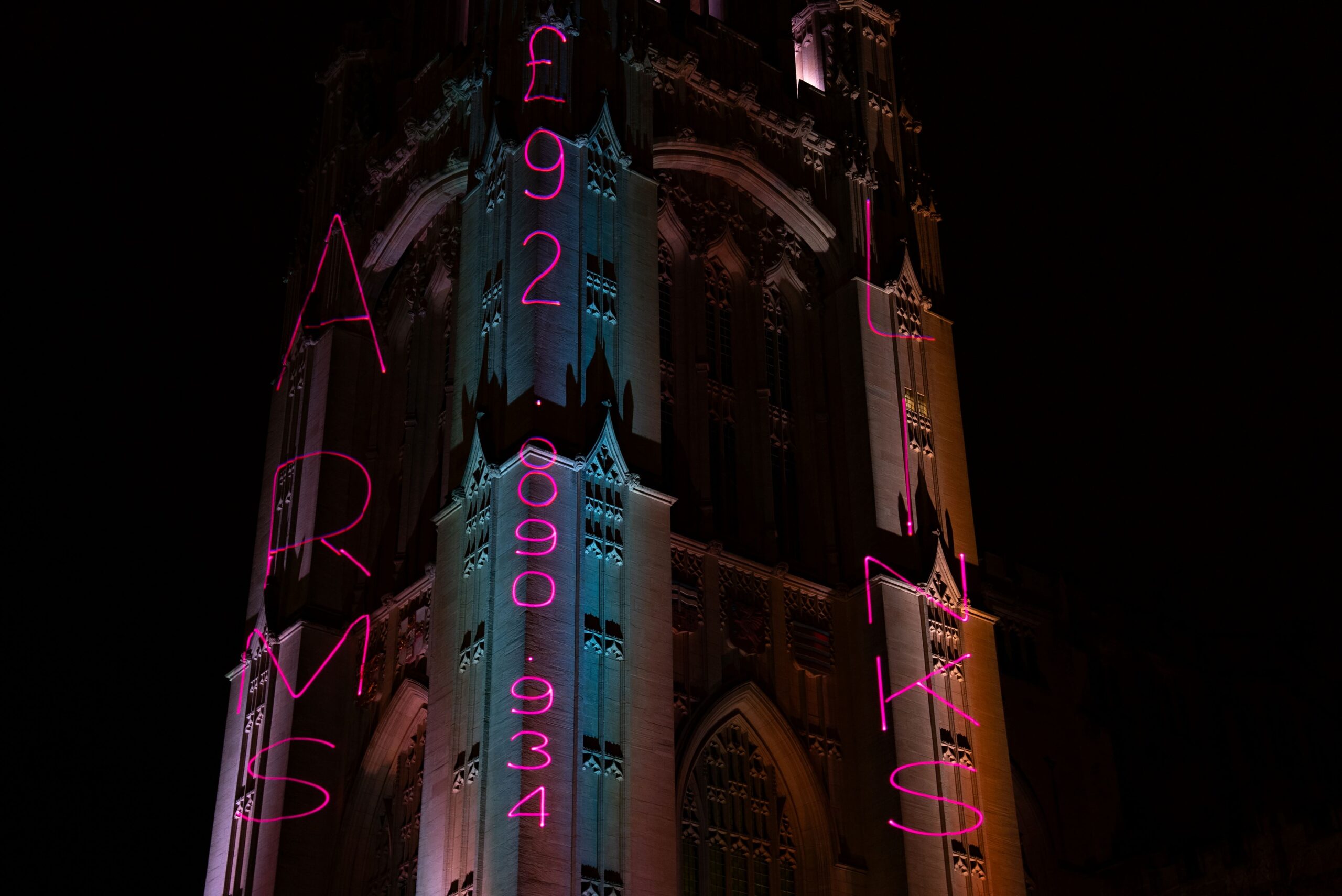 Pink projection on Wills Memorial Tower vertically reading: Arms £92,890,934 Links