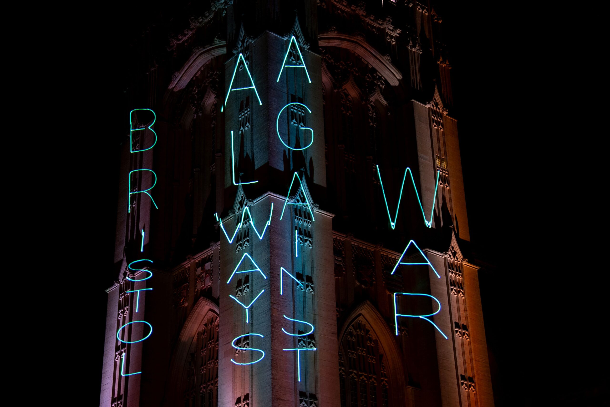 Blue projection on Wills Memorial Tower vertically reading: Bristol always against war