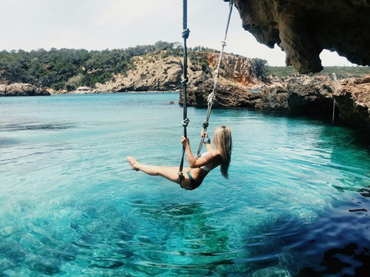 woman on a hammock above the crystal clear waters of a beach in Ibiza