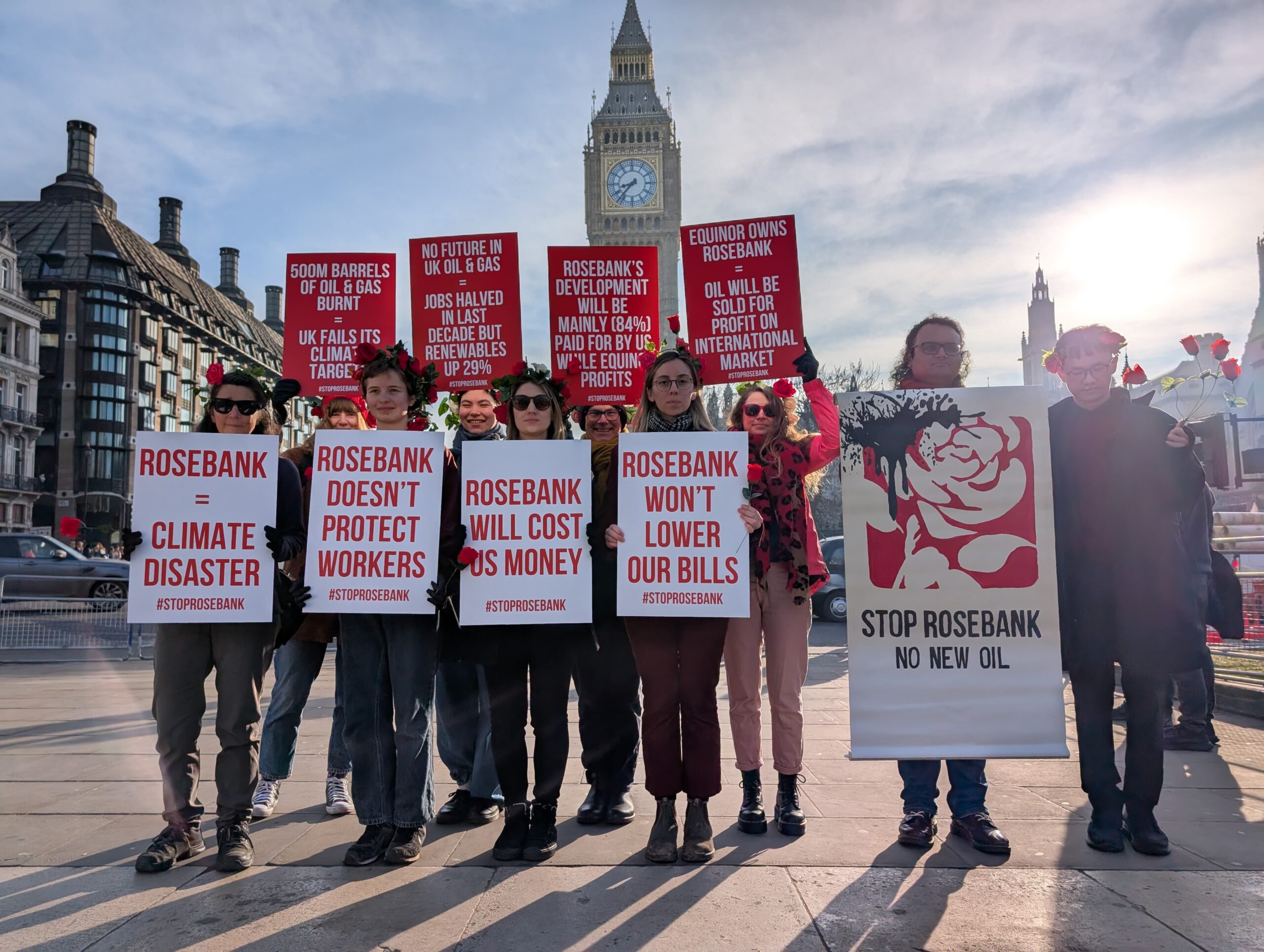 Campaigners adorned in roses hold placards with Big Ben in the background. These read from left to right, top to bottom: "500m barrels of oil & gad burnt = UK fails its climate targets", "No future in UK oil & gas = jobs halved in last decade but renewables up 29%", "Rosebank's development will be mainly (84%) paid for by us while Equinor profits", "Equinor owns Rosebank = oil will be sold for profit on international market", "Rosebank = climate disaster", "Rosebank doesn't protect workers", "Rosebank will cost us money", and "Rosebank won't lower our bills". The final poster to the right displays the Labour Party rose logo dripping in oil with the caption "Stop Rosebank - no new oil". 