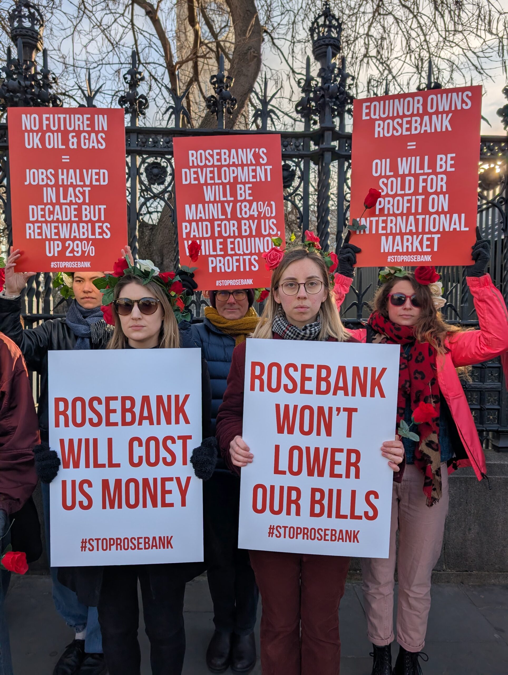 Climate campaigners with roses in their hair raise red and white placards reading: "No future in UK oil & gas = jobs halved in last decade but renewables up 29%", "Rosebank's development will be mainly (84%) paid for by us while Equinor profits", "Equinor owns Rosebank = oil will be sold for profit on international market", "Rosebank = climate disaster", "Rosebank doesn't protect workers", "Rosebank will cost us money", and "Rosebank won't lower our bills".